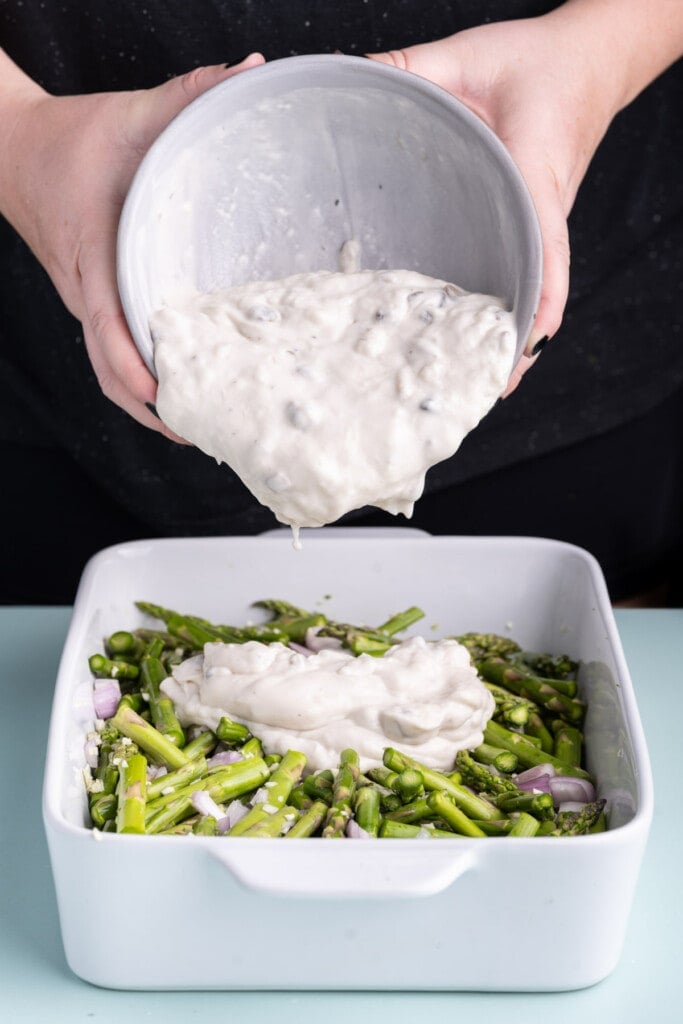 Pouring cream of mushroom soup over asparagus, shallots, and garlic