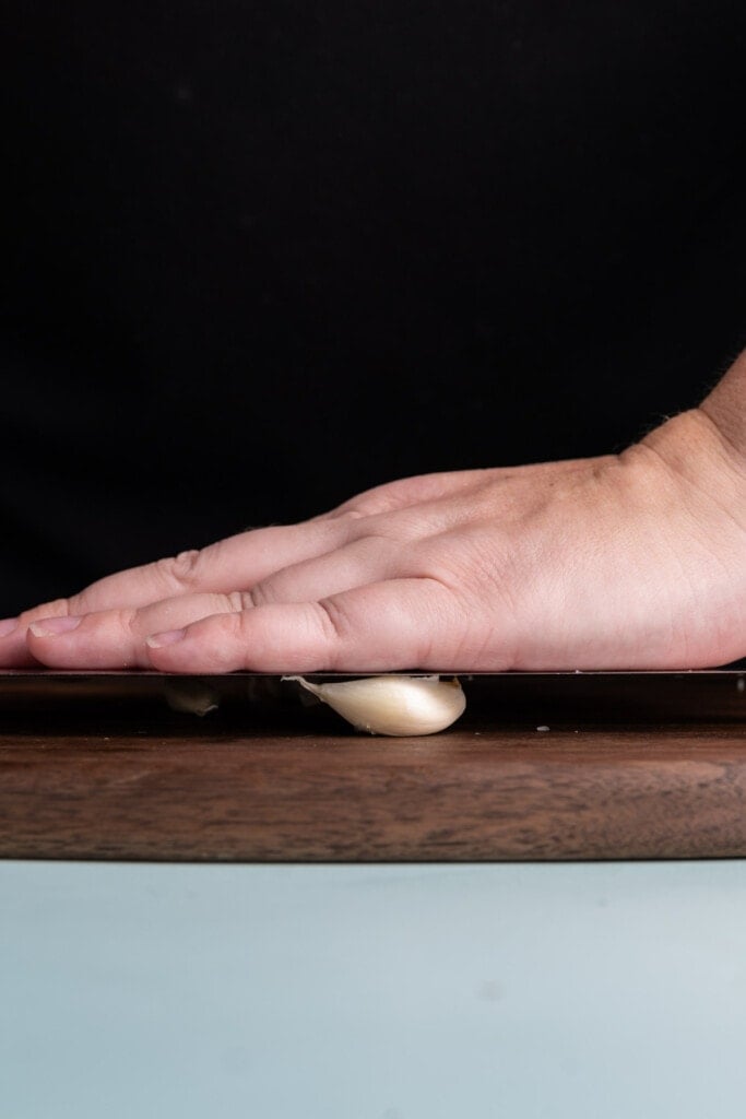 Using the flat side of a knife to crush garlic