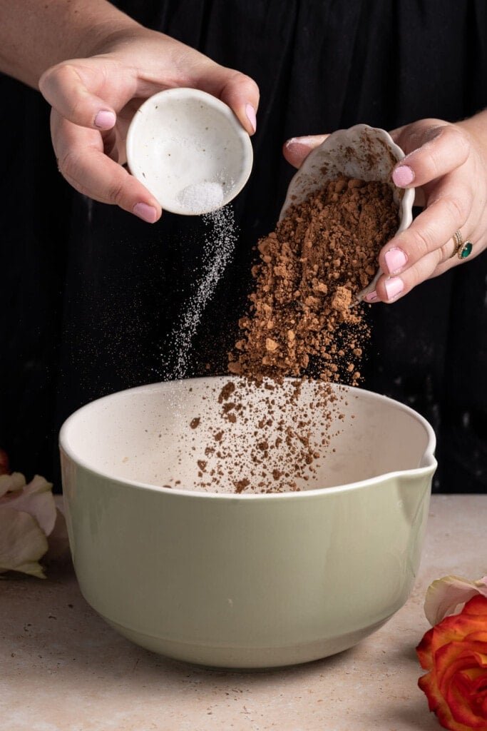 Adding cocoa powder and salt to a mixing bowl to make brownie batter.