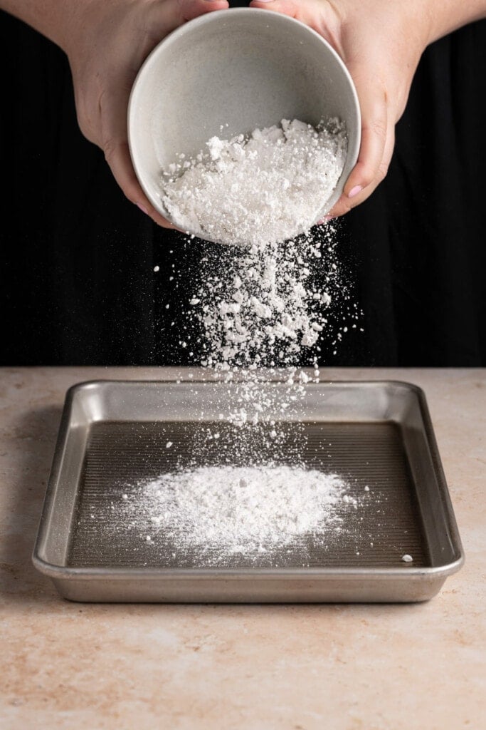 Adding flour to a baking sheet to heat treat it in the oven.