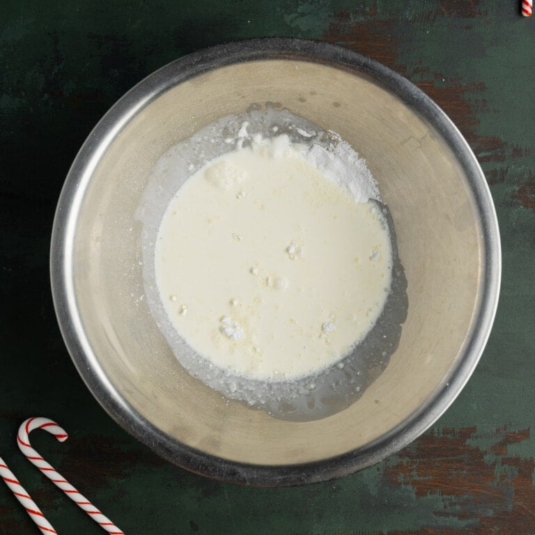 Heavy cream, powdered sugar, and peppermint extract in a stainless steel mixing bowl