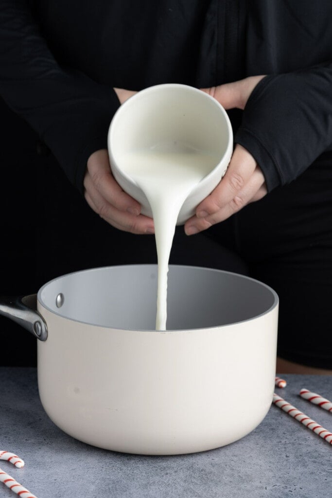 Pouring milk into a small pot to heat with chocolate chips.