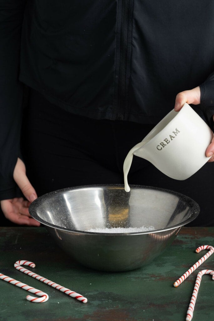 Adding heavy whipping cream to stainless steel bowl with powdered sugar.