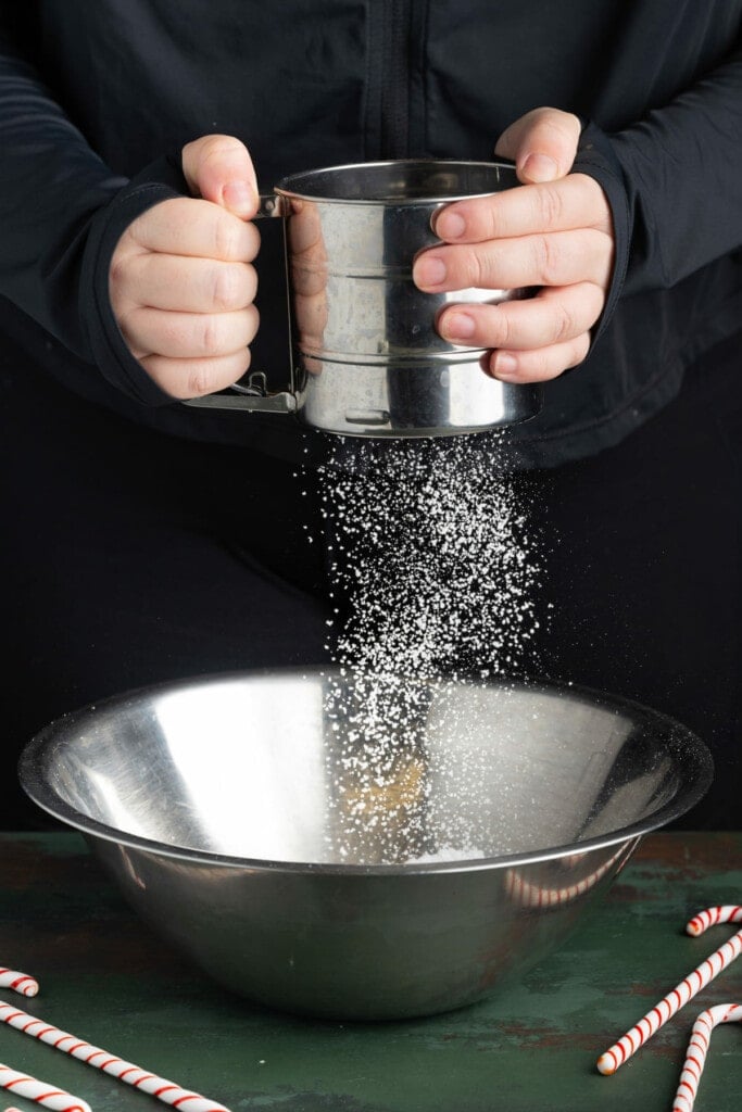 Sifting powdered sugar into metal bowl with whipped cream.