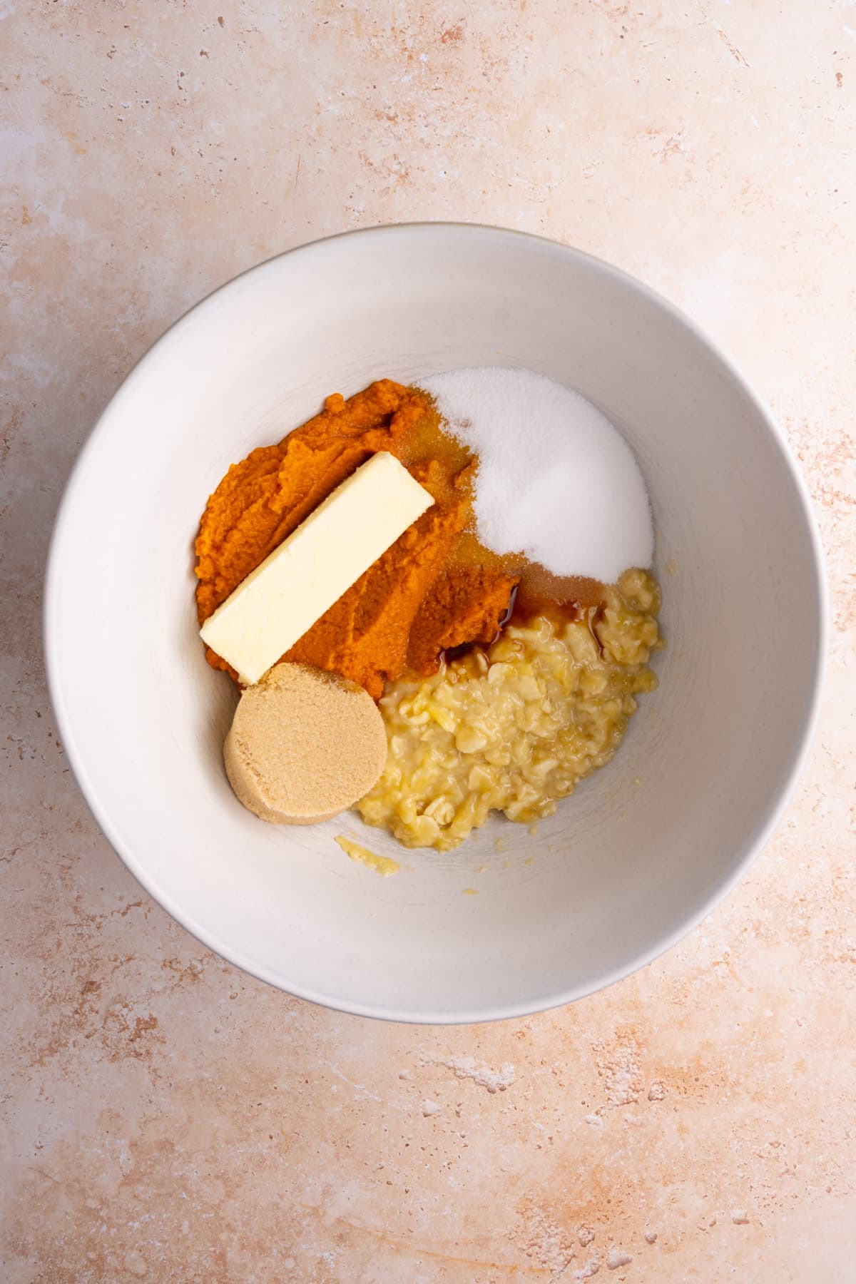 Smashed banana, softened unssalted butter, pumpkin puree, vanilla extract, brown sugar, and white sugar in a bowl