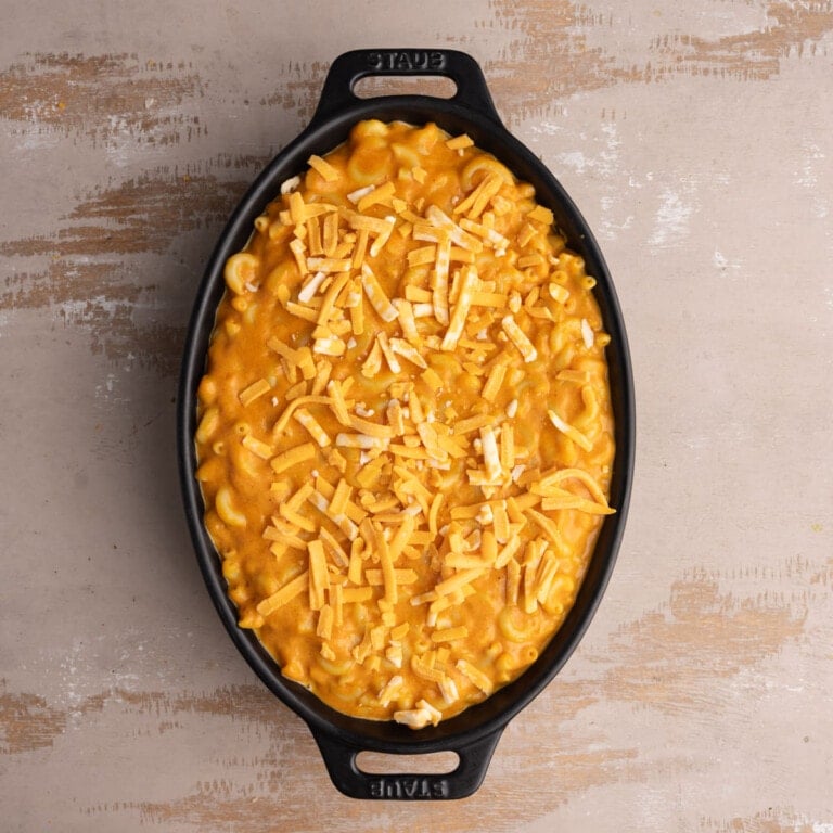 Adding cheese on top of pumpkin mac and cheese in baking dish