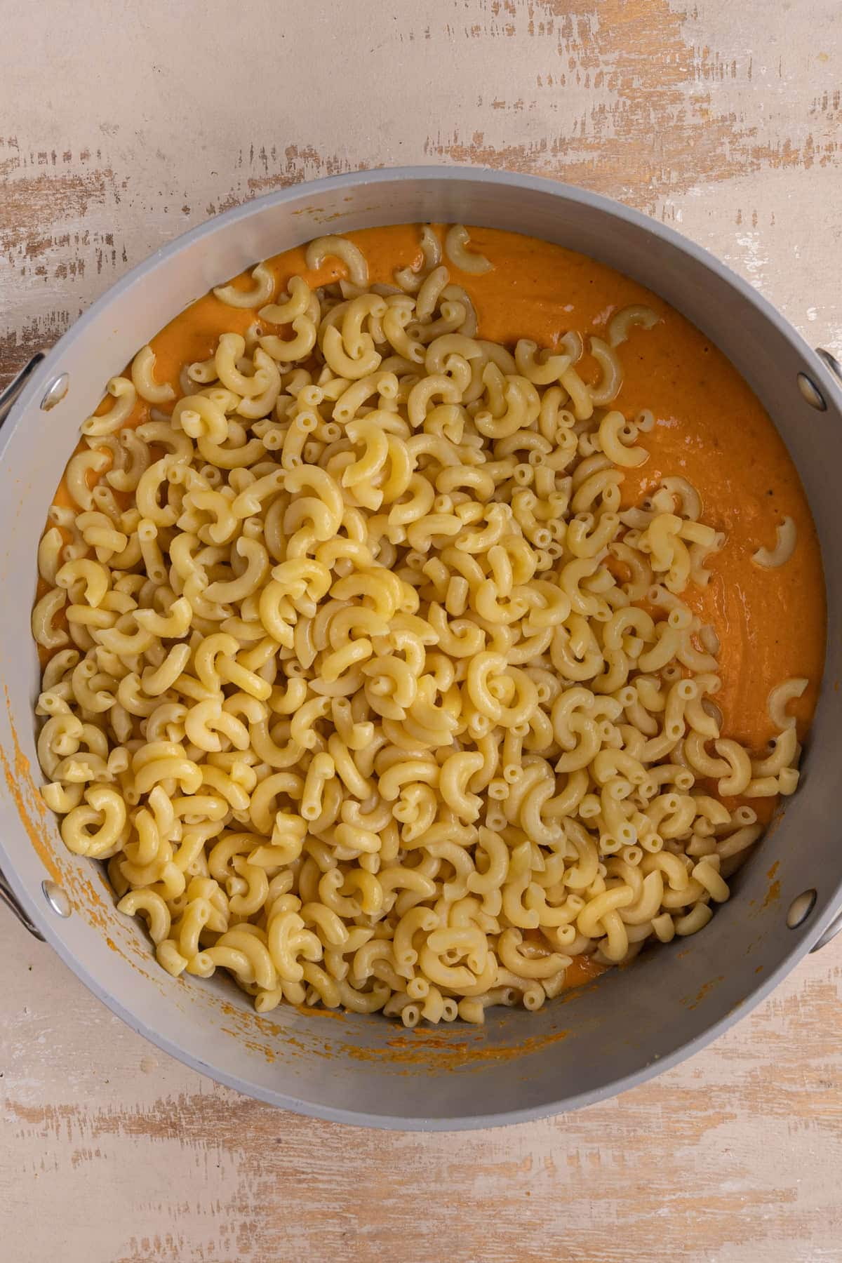 Adding cooked macaroni to pumpkin cheese sauce