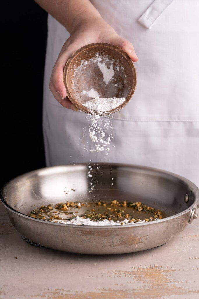 Adding flour to form a roux for a creamy sauce.