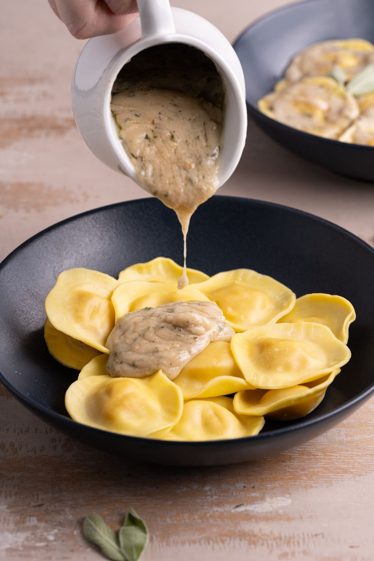 Adding creamy coconut sage sauce to cooked butternut squash ravioli