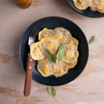 Plate of ravioli with creamy coconut sage sauce and a wooden fork