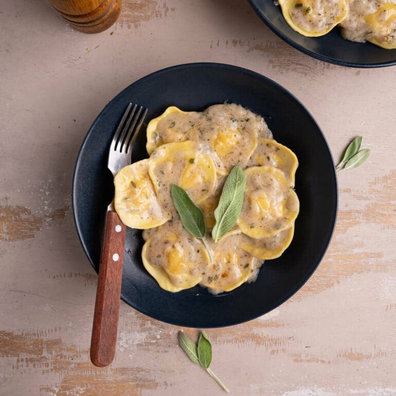 Plate of ravioli with creamy coconut sage sauce and a wooden fork