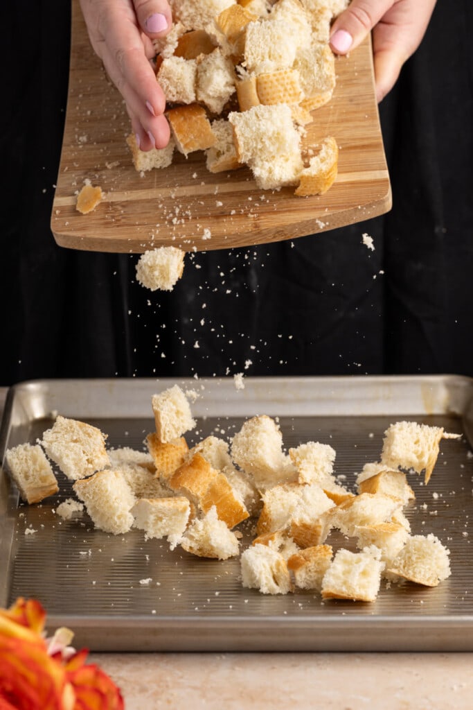 Adding cubed bread to a baking sheet to toast