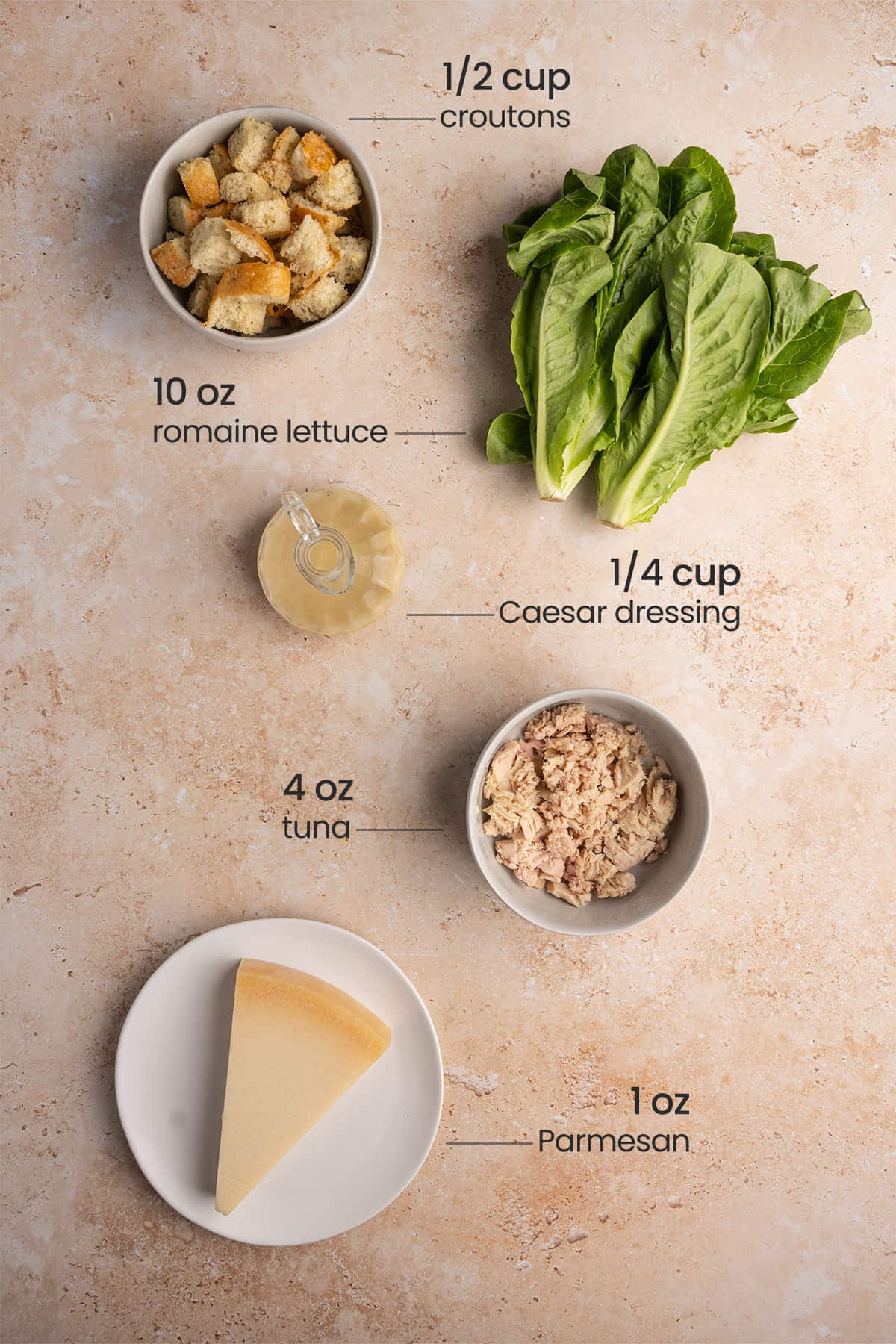 All ingredients for Tuna Caesar Salad including croutons, Romaine lettuce, Caesar dressing, canned tuna. and Parmesan cheese