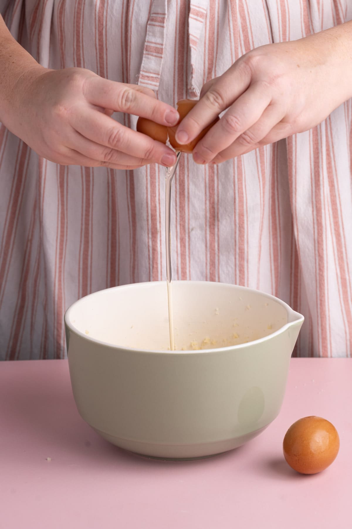 Cracking an egg into a mixing bowl with sugar, butter, and vanilla extract.