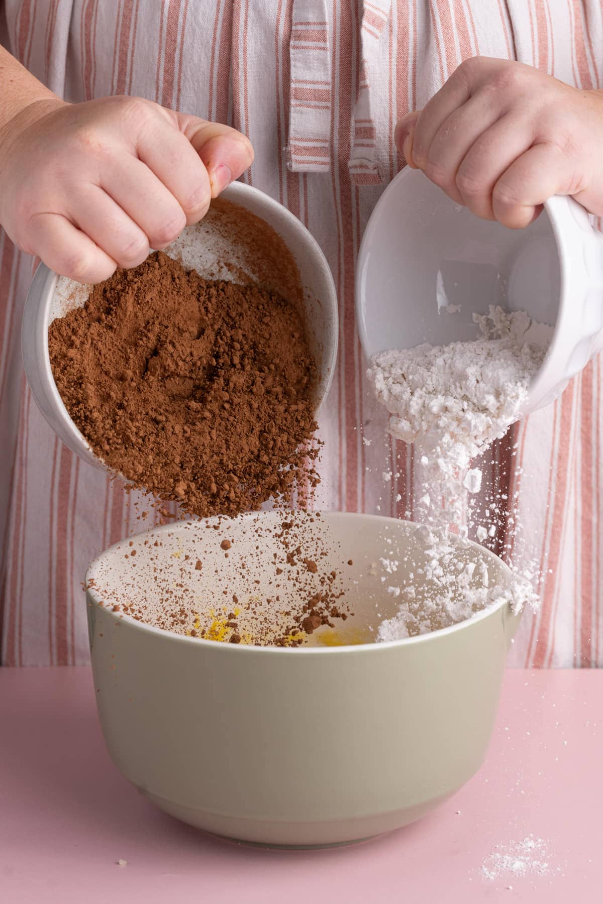 Adding cocoa powder and flour to a mixing bowl with wet ingredients.