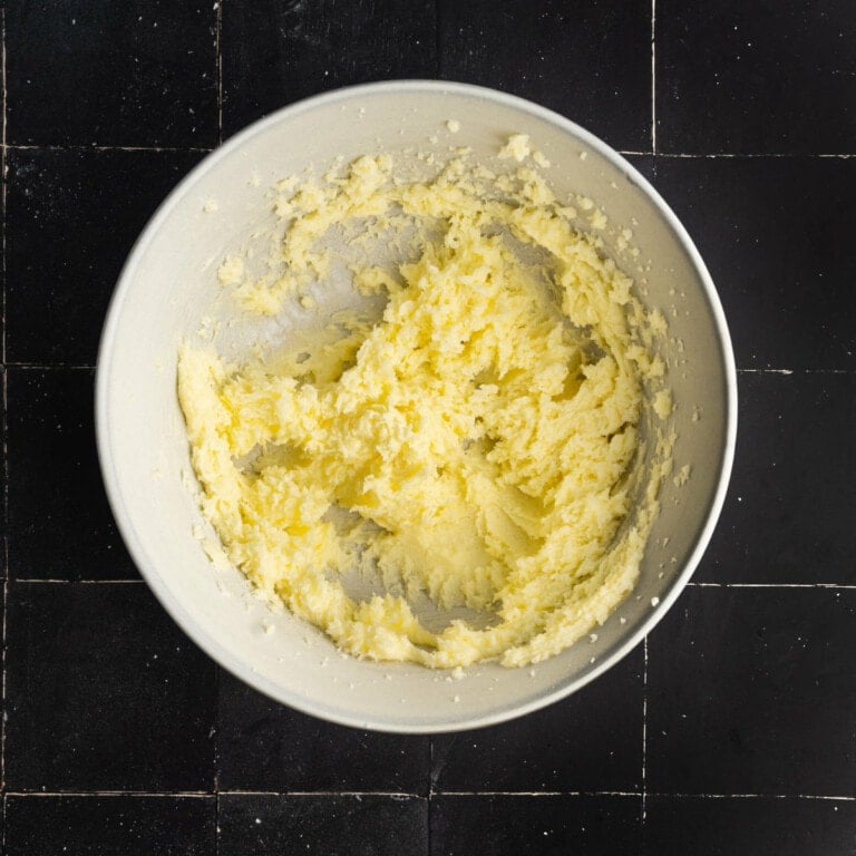 Butter and granulated sugar creamed together in a mixing bowl on a black background.