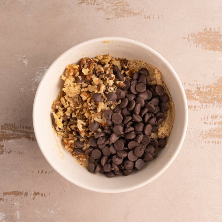 Cookie dough in a bowl with a generous amount of dark chocolate chips and chopped walnuts.