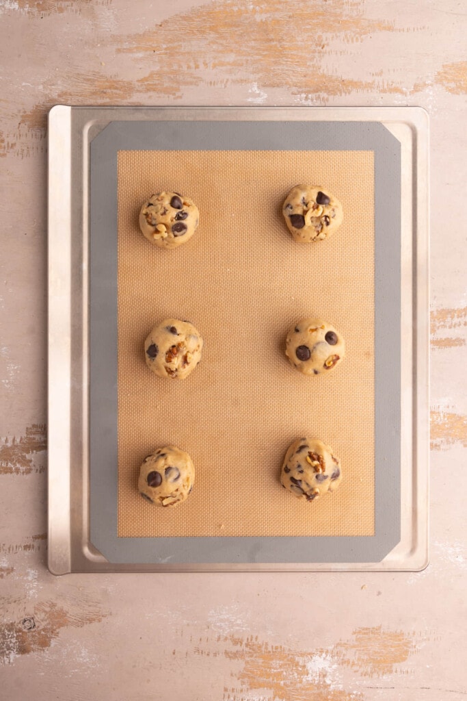 Chocolate Chip Walnut cookie dough shaped and placed on a lined baking sheet ready for the oven.