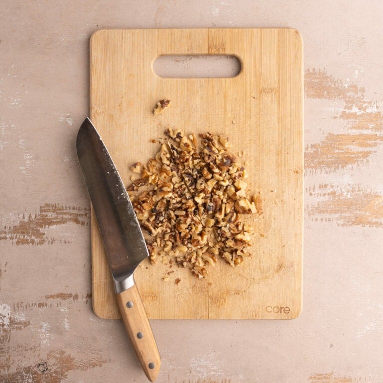 Chopped walnuts on a cutting board with a knife.