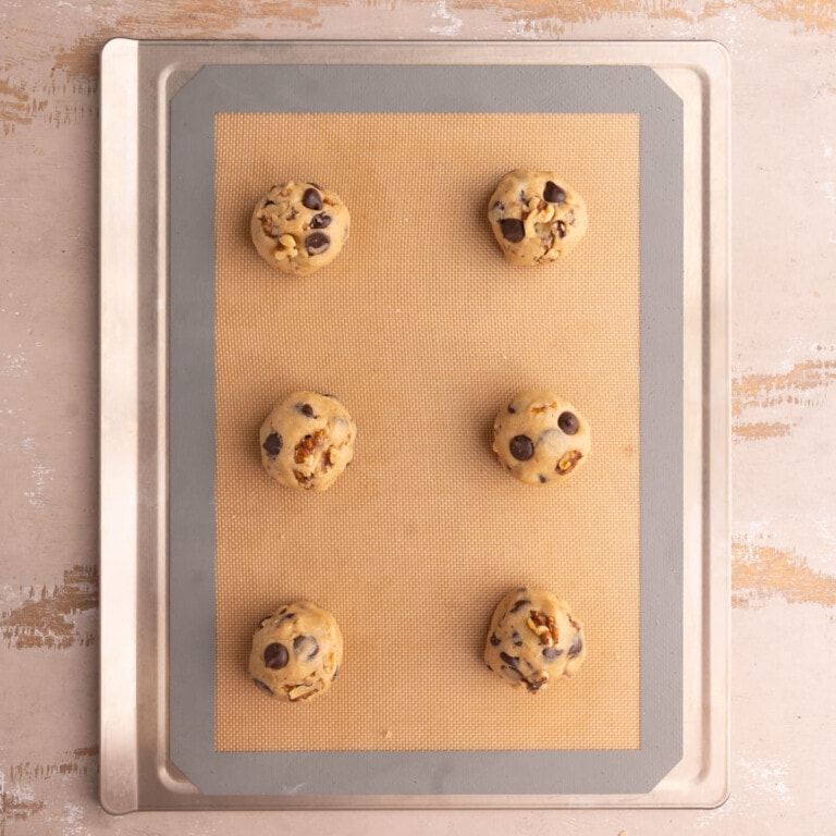 Baking sheet lined with a reusable baking mat with six cookie dough balls on it.
