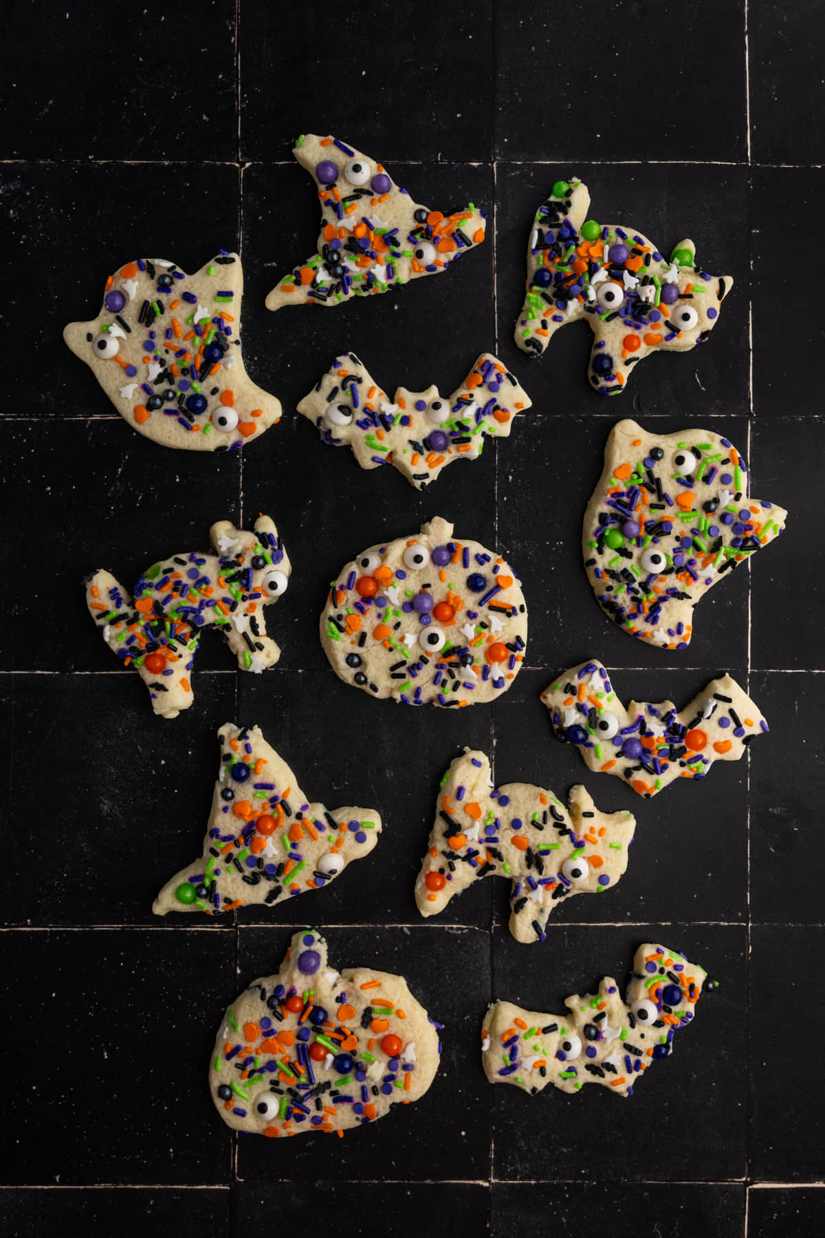 A variety of different Halloween shaped sugar cookies on a black surface.