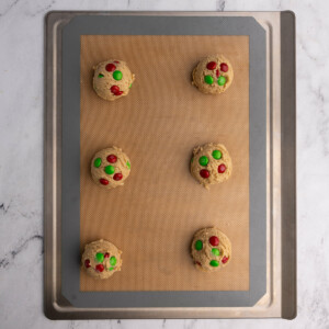 Lined baking sheet with six balls of M&M cookie dough on it.