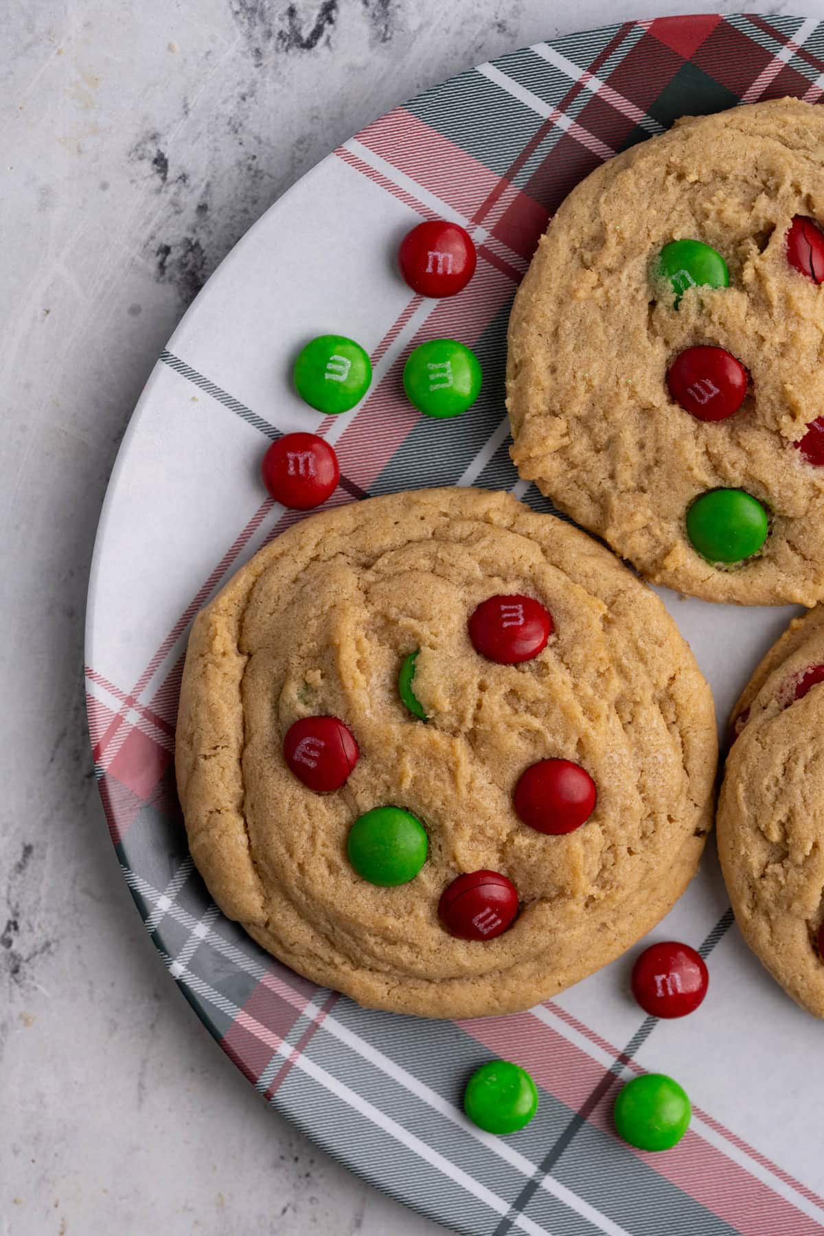 Overhead image of Christmas cookies on a red and green plate surrounded by M&M's.