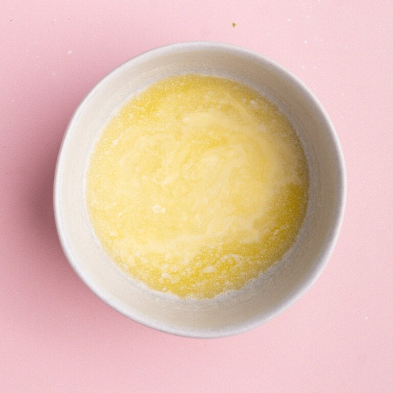 Melted butter in a small bowl on a pink background.