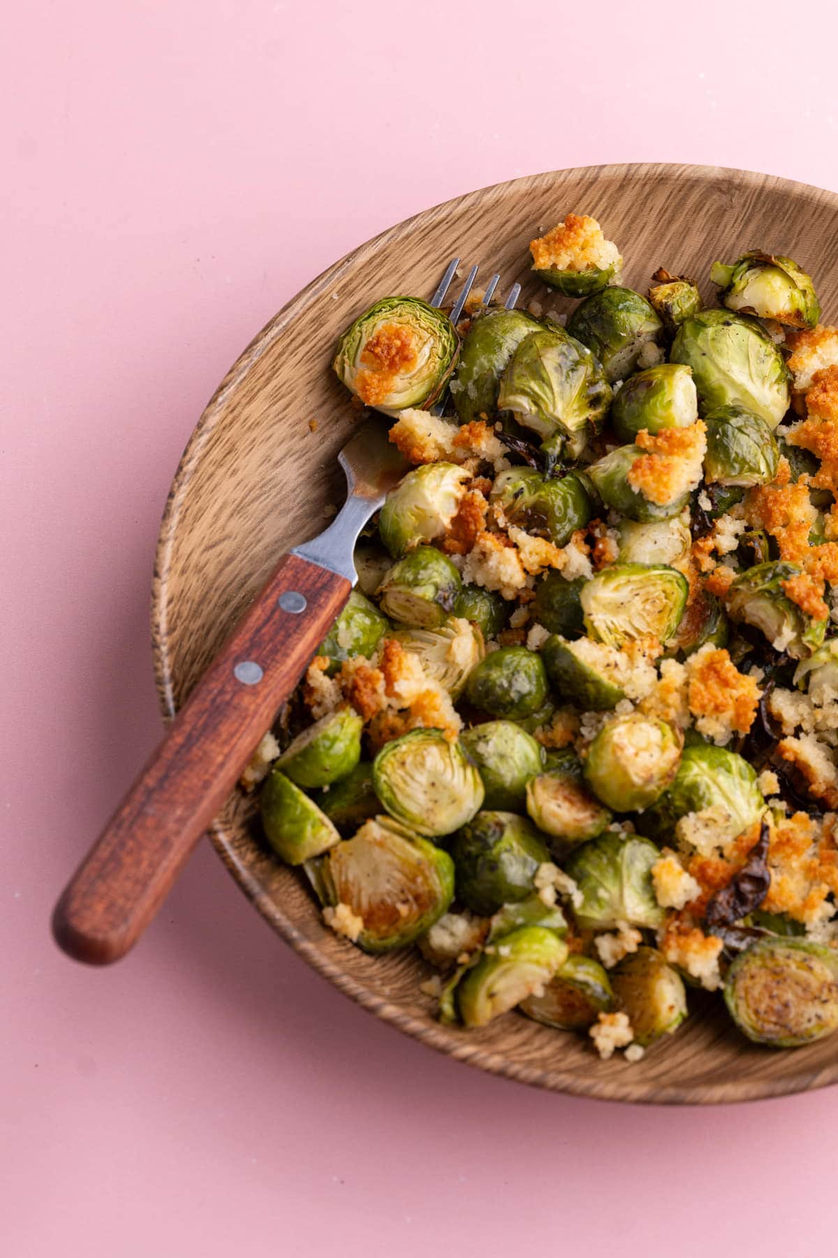 Parm Crusted Brussels Sprouts in a wooden bowl with a wooden serving fork.