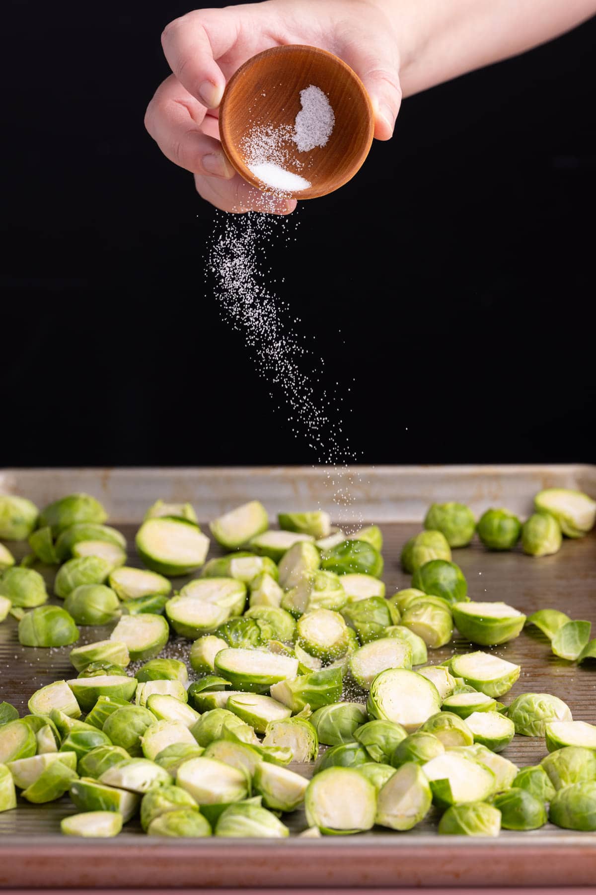 Adding seasoning to brussels sprouts on a baking tray.