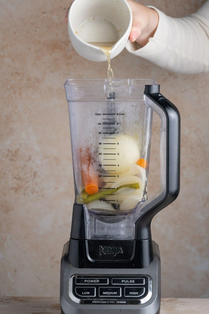 Adding broth to a blender with boiled vegetables to make a veggie puree.