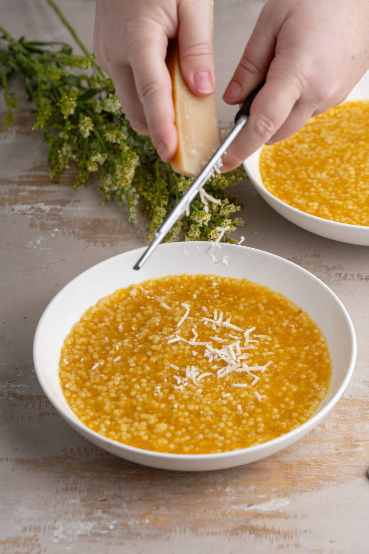 Grating Parmigiano reggiano over top vegetable pastina soup.