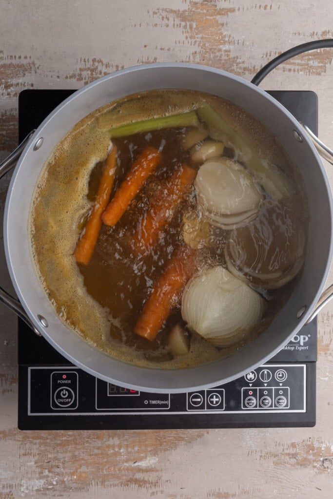 Boiling carrots, celery, onions, and garlic in vegetable broth for pastina soup.