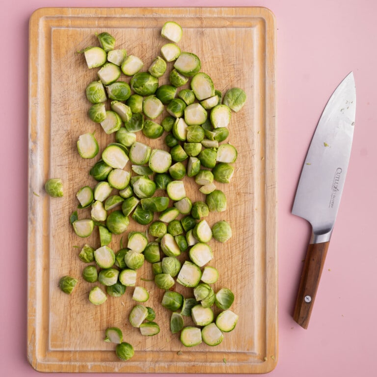 Chopping board with prepped and halved brussels sprouts ready for roasting.
