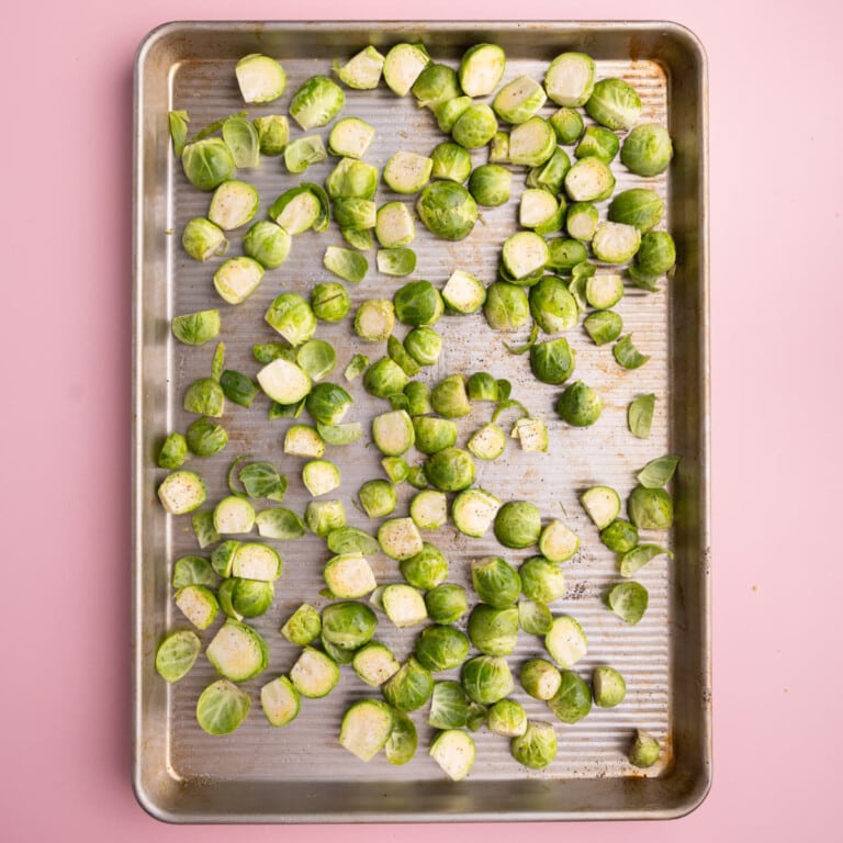 Brussels sprouts with salt, pepper, and olive oil on a baking sheet.