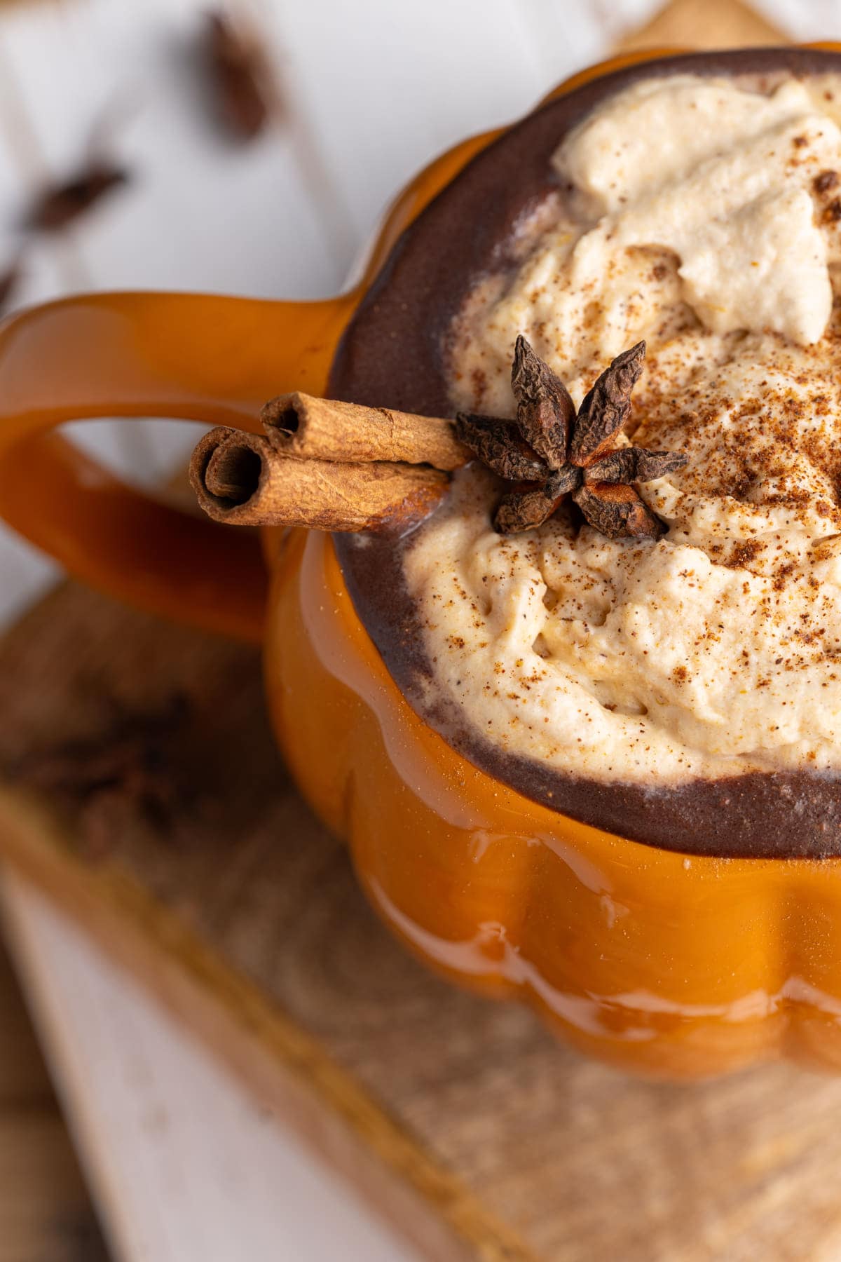 Close up of star anise and cinnamon stick garnishing hot chocolate in a pumpkin mug