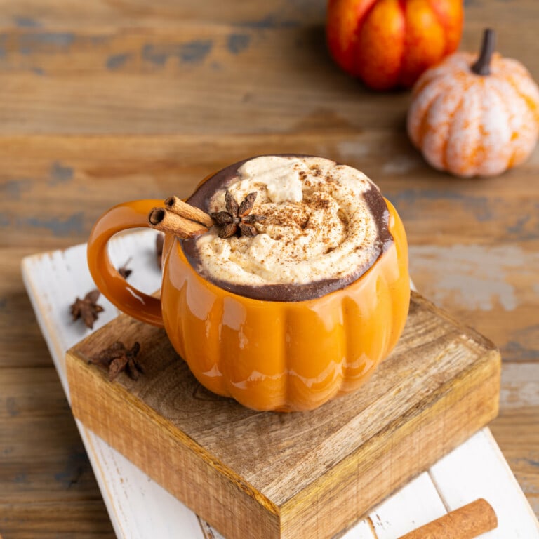 Pumpkin shaped mug filled with pumpkin spice hot chocolate with little pumpkins in the background