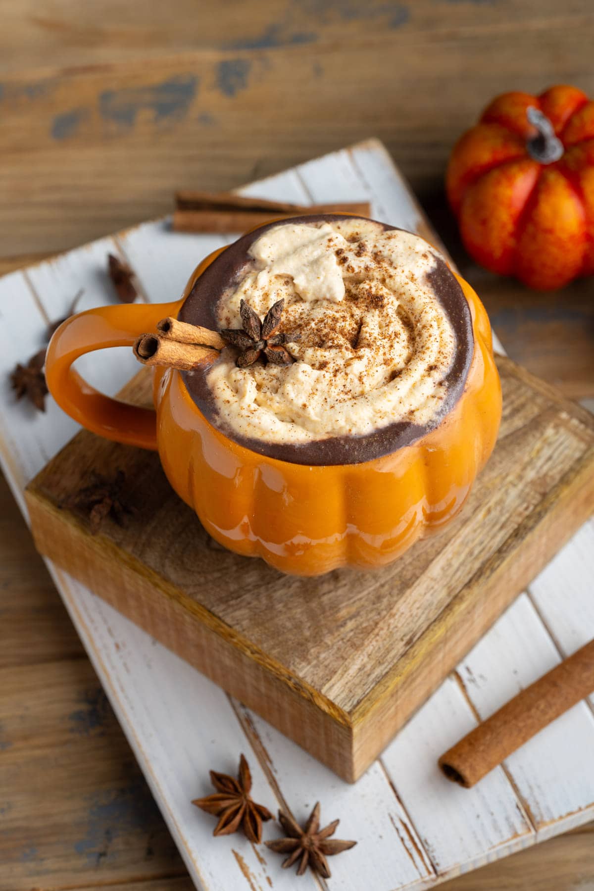 pumpkin shaped mug with pummpkin spice hot chocolate topped with whipped cream and Fall spices