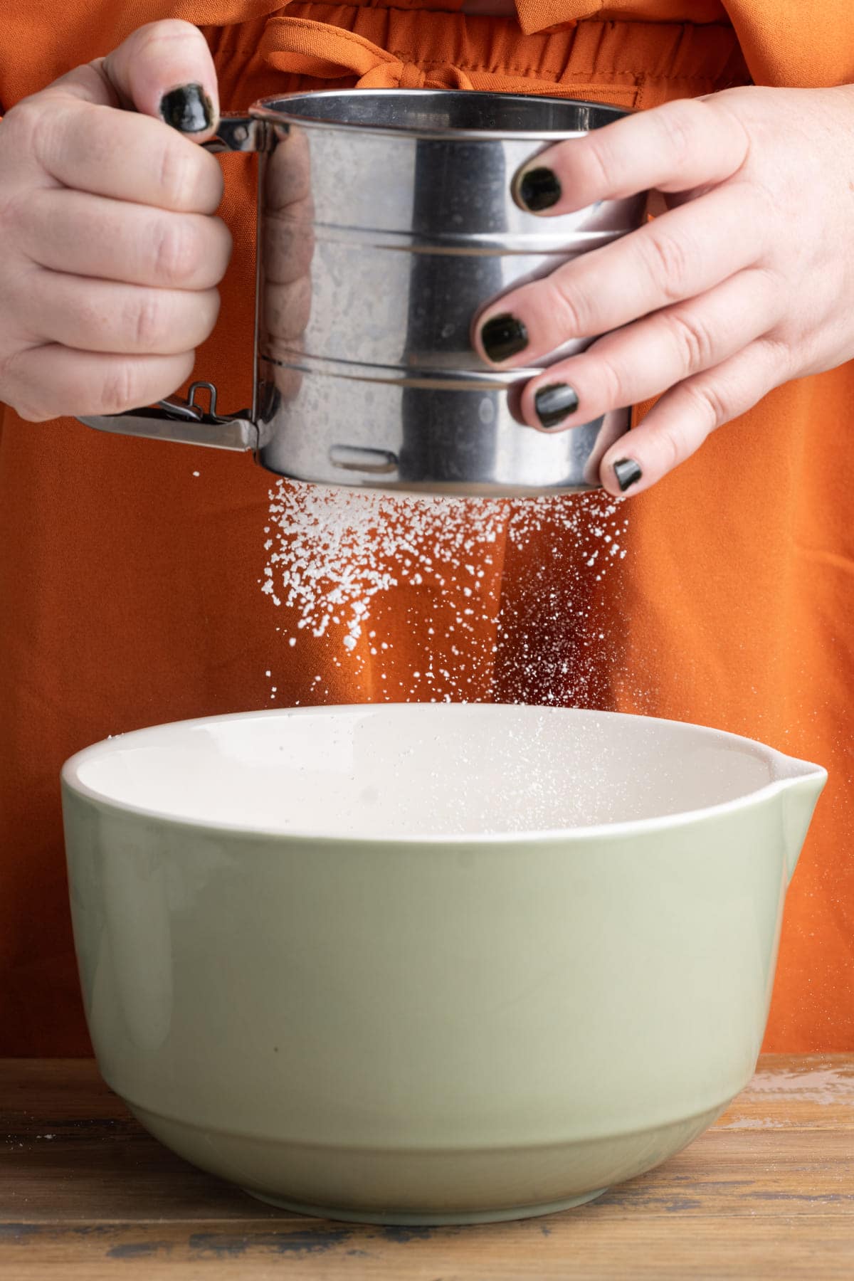Sifting powdered sugar into a ceramic mixing bowl with cold whipping cream