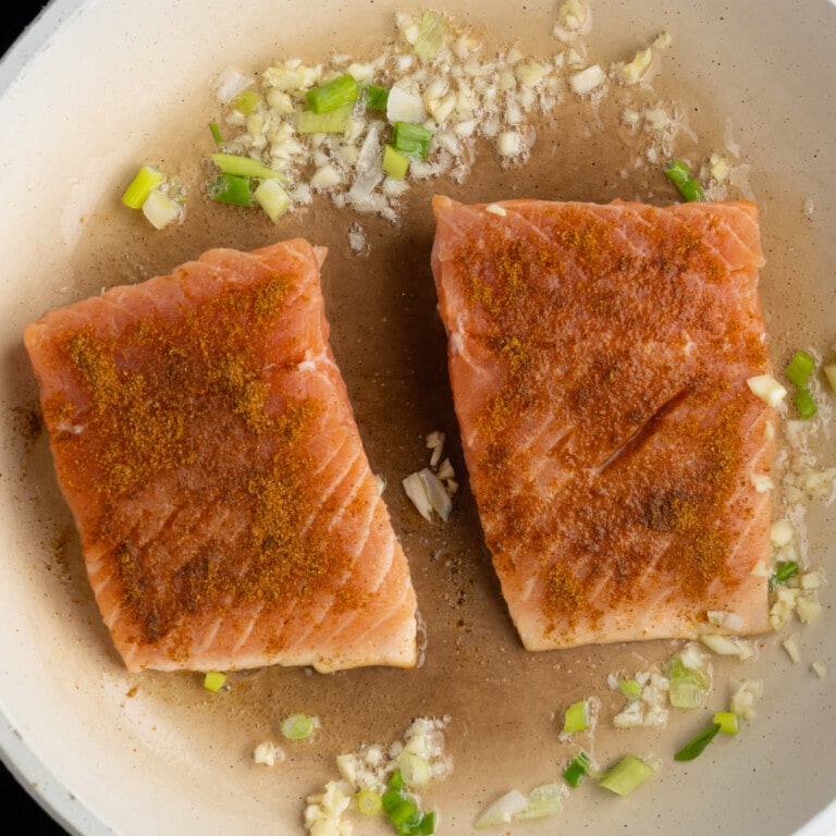 Garlic, shallots, and salmon in pan with hot oil seasoned with lemon juice and Cajun seasoning