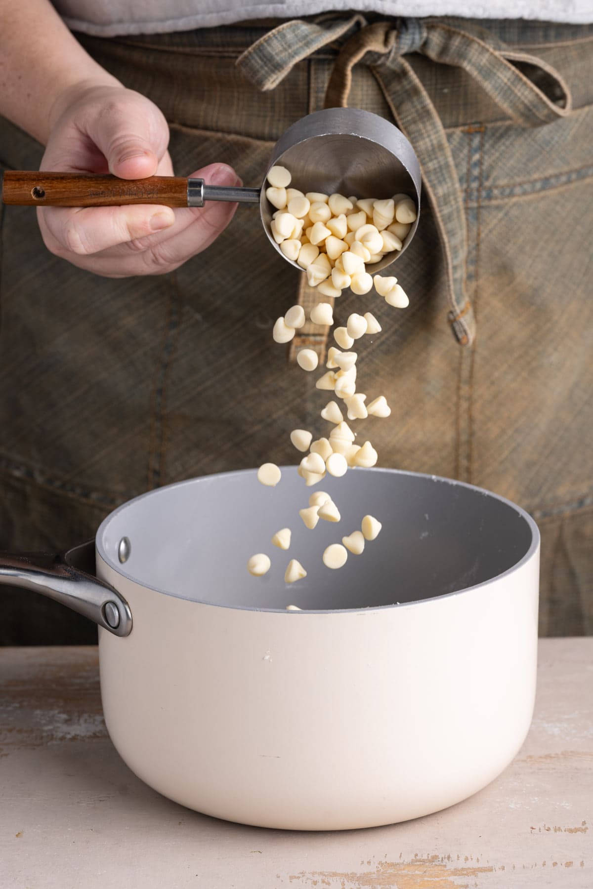 Adding white chocolate chips to a pot with butter to melt together