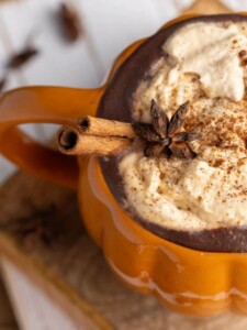 Close up of star anise and cinnamon stick garnishing hot chocolate in a pumpkin mug