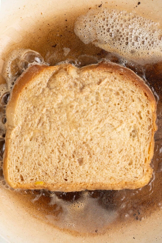 Frying French toast in sizzling butter on the first side.