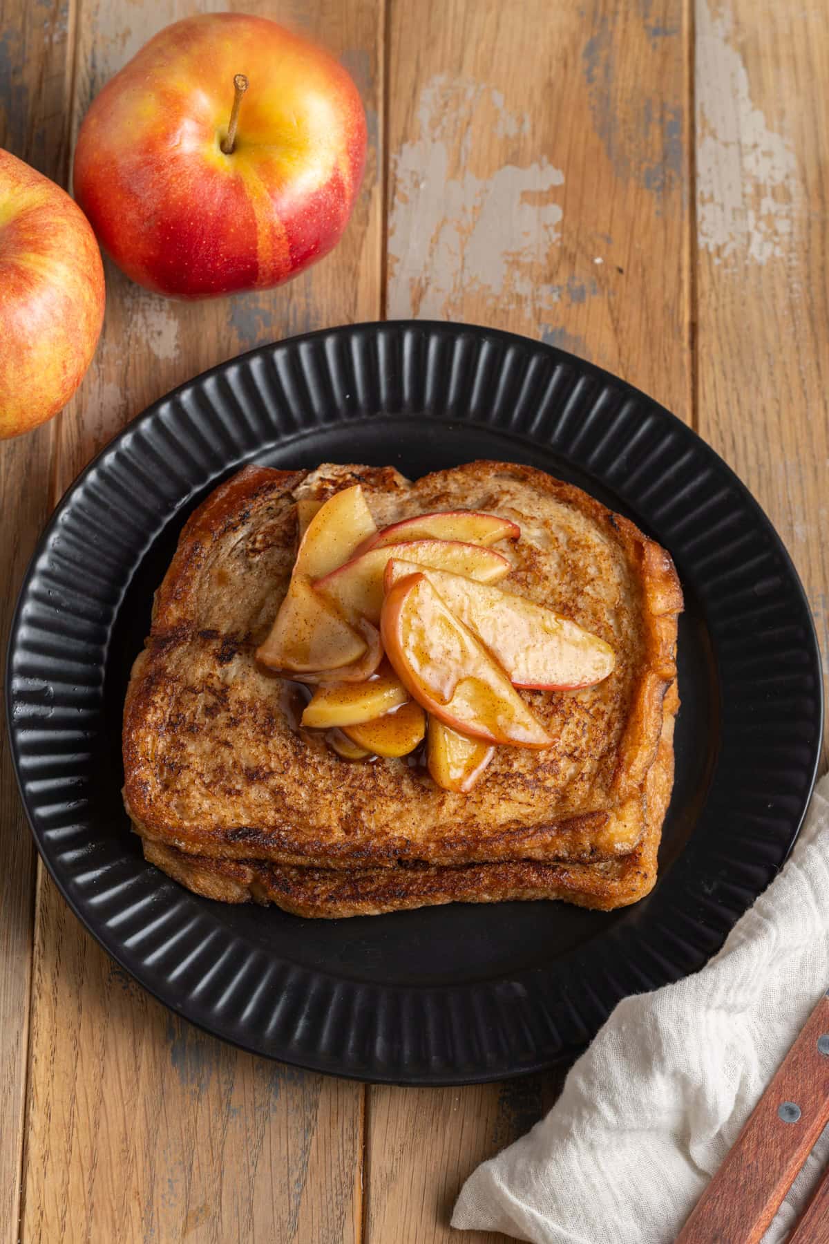 Two slices of apple cider French toast plated with sauteed cinnamon apples on top. 