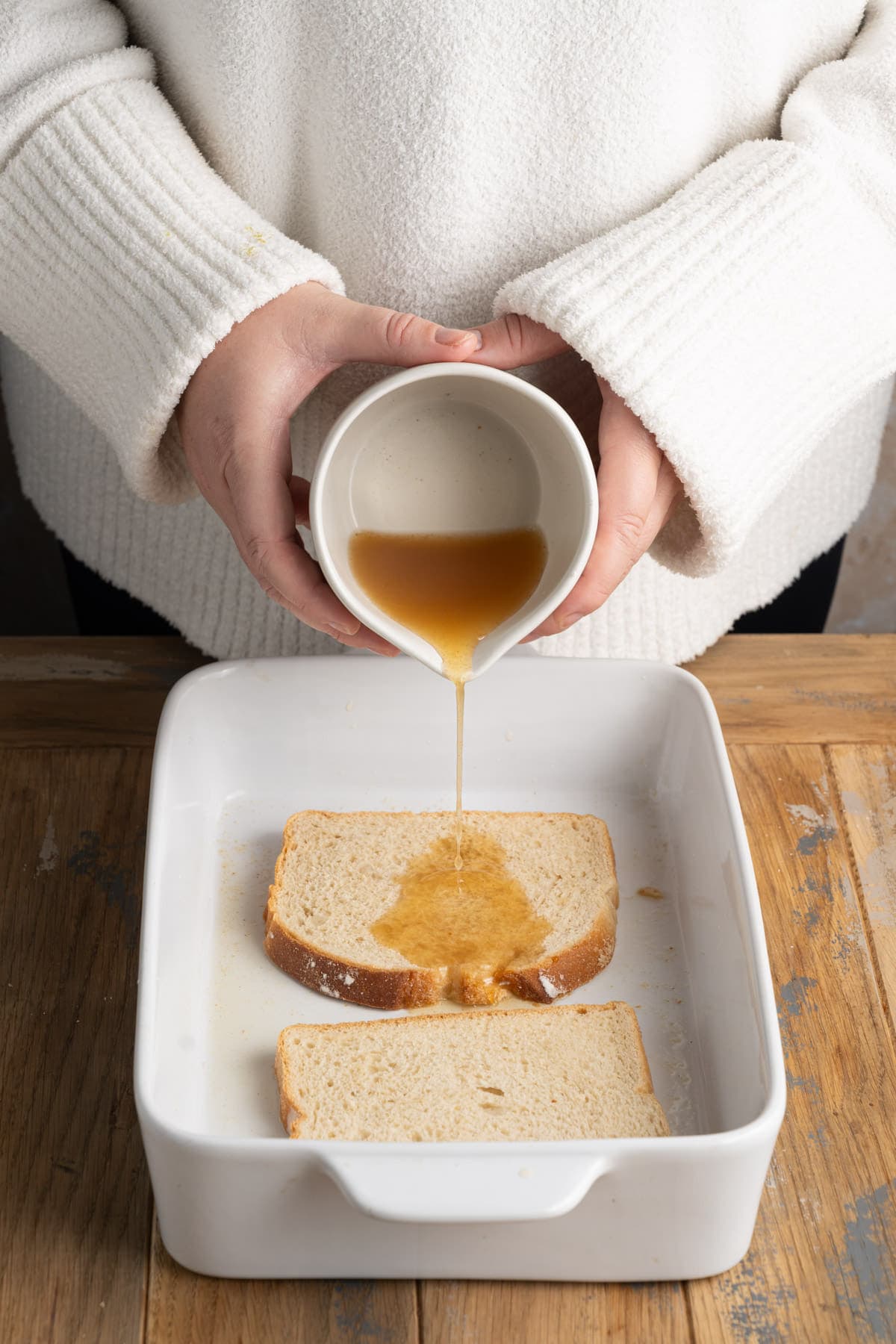 Pouring apple cider over stale bread in a baking dish. 