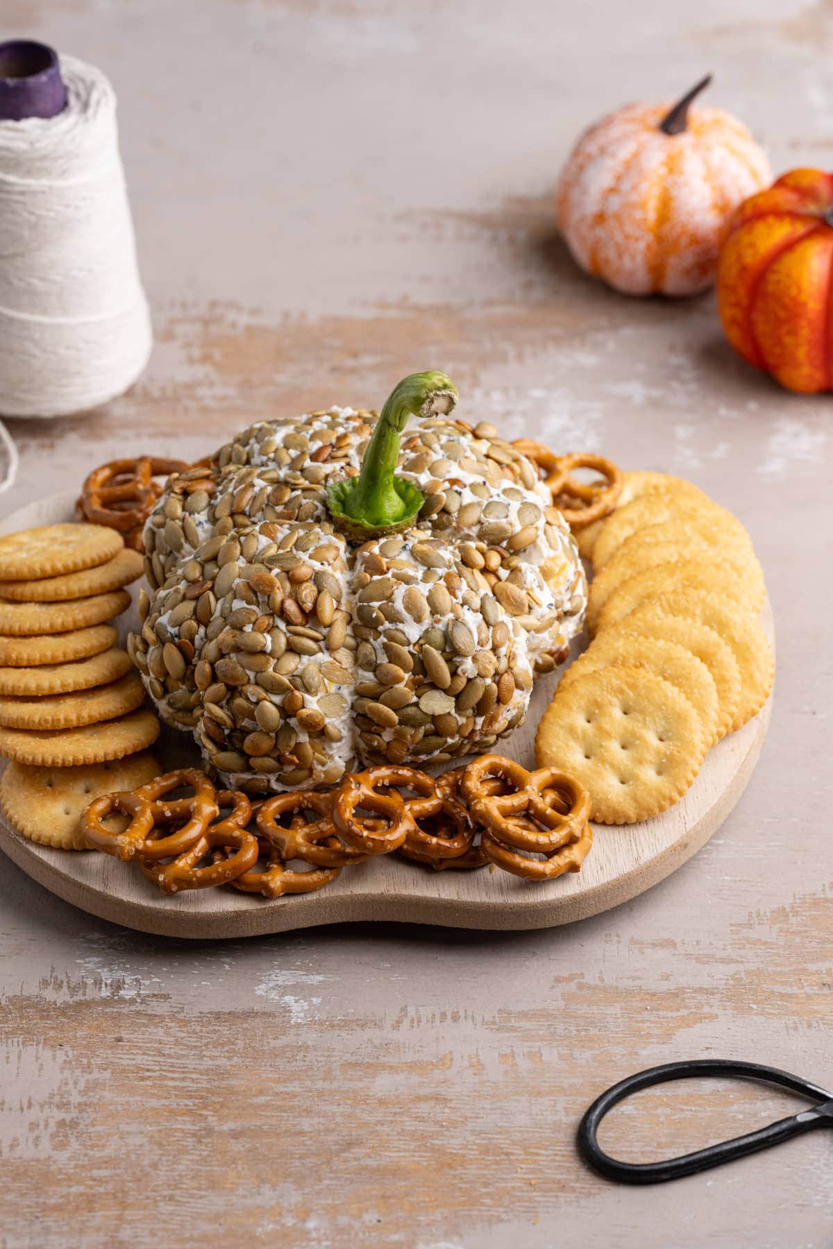 Cheese Pumpkin on a wooden board surrounded by crackers and pretzels. 