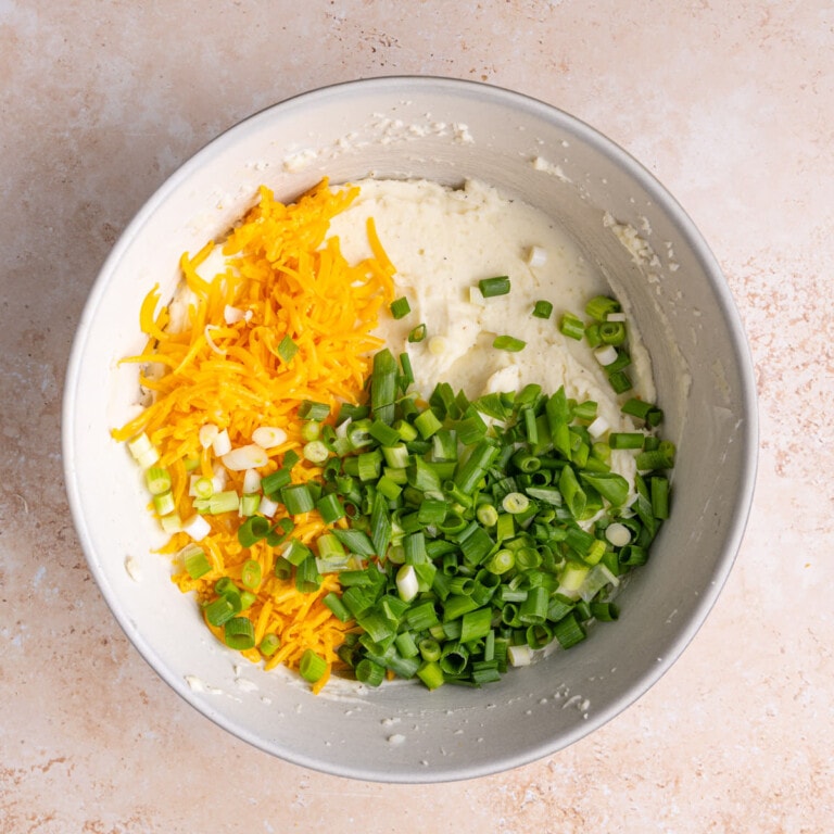 Large bowl of creamy mashed potatoes with shredded cheese and green onions.