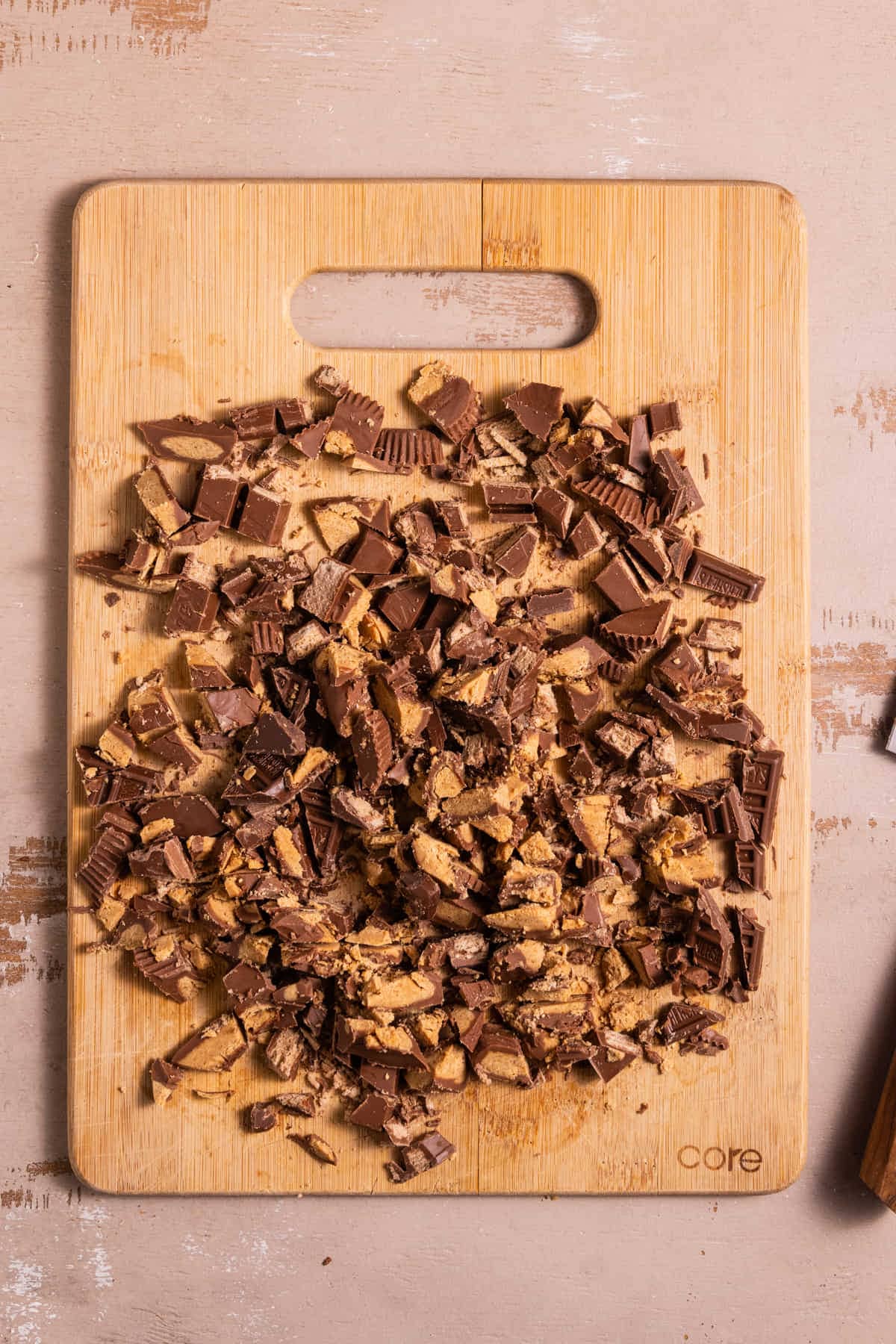 Kit Kats, Reese's cups, and Hersheys chocolate roughly chopped on a cutting board.