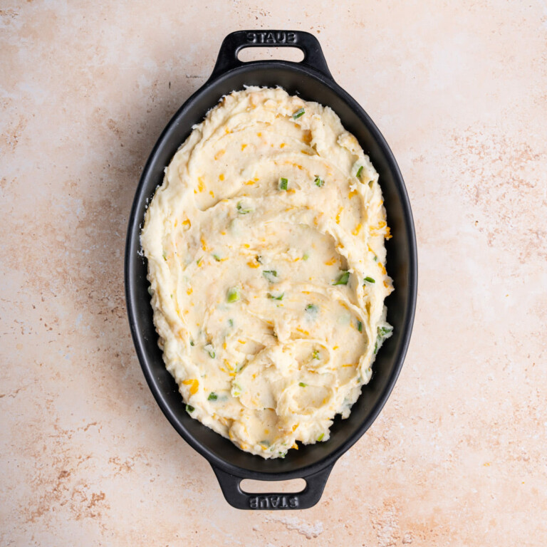 Creamy mashed potatoes with cheese and green onions in a casserole dish.