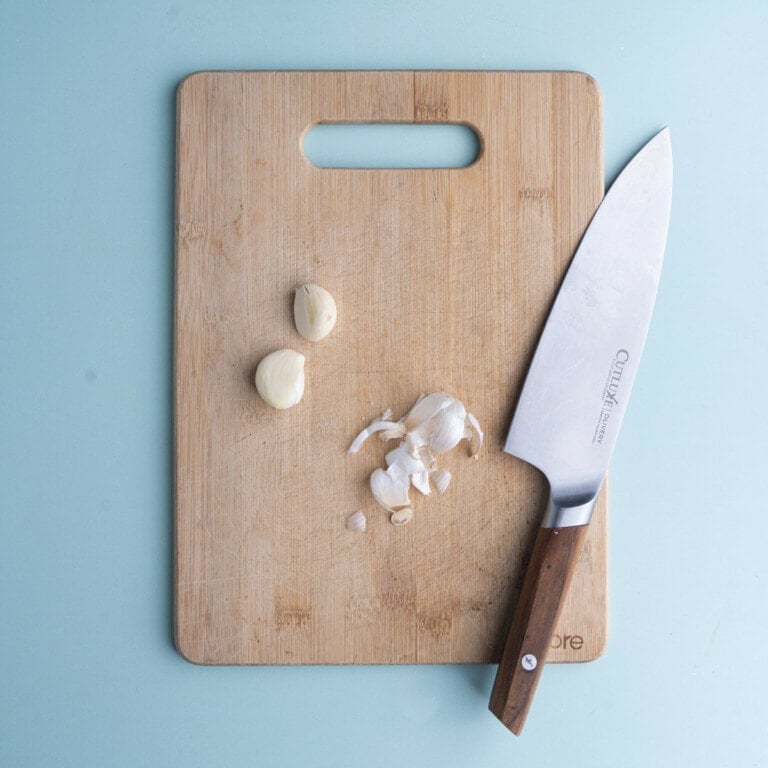 Two cloves of garlic peeled and set on a chopping board.